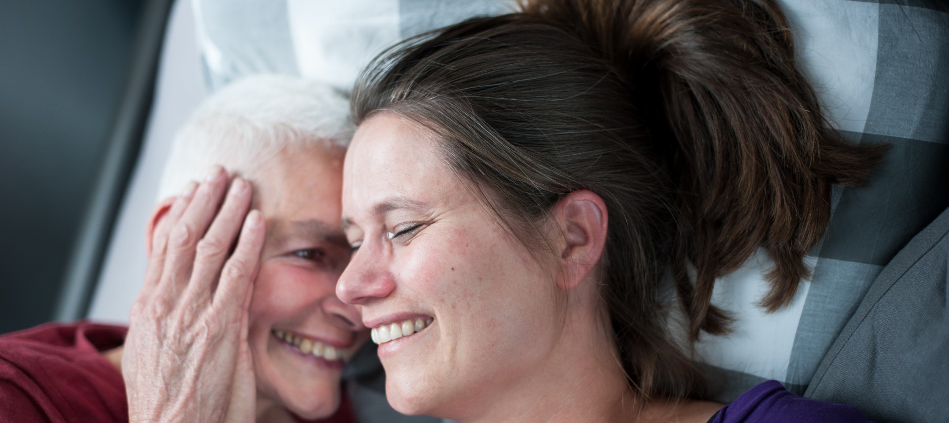 oude-vrouw-knuffelt-vrolijk-jongere-vrouw-op-bed-patient